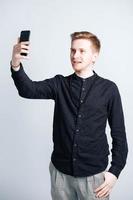 Young man in a black shirt with a smartphone in his hands on a white background. Copy, empty space for text photo