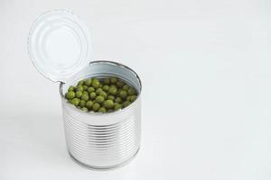 Canned green sweet peas in an open aluminum metal can on a white table. Copy, empty space for text