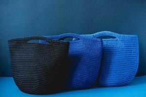 Three blue knitted handmade bag on a blue background. Copy, empty space for text photo