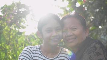 Senior grandmother and adorable granddaughter posing hugs each other and looking at camera. video