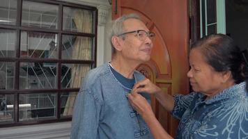 Elderly grandmother is buttoning shirt and caring her husband before leaving home. video