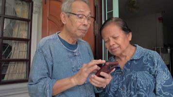 homme âgé enseignant à sa femme à l'aide d'une application mobile sur smartphone pendant son séjour à la maison.