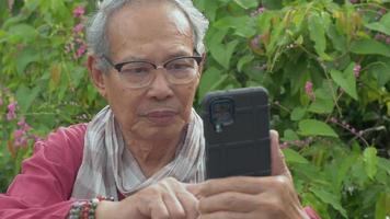 senior pensioen man met behulp van smartphone selfie foto te nemen in de tuin. video