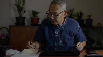 empresario anciano escribiendo en papeleo y abierto para comenzar a usar una computadora portátil en casa. video