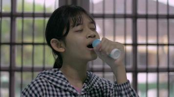 une adolescente joyeuse chante en utilisant un flacon pulvérisateur au lieu d'un microphone.