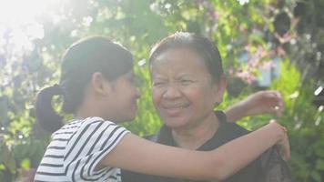 Elderly grandmother hugs her adorable granddaughter in the garden at home. video