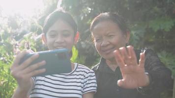 Teen girl and her senior grandmother enjoy talking to their family with video chat online from mobile smartphone.
