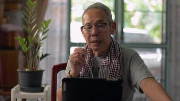 retraité senior parlant avec des amis à l'aide d'un petit appareil de conversation via un appel vidéo sur une tablette numérique à la maison.