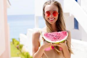 All Inclusive Cheap Summer Holidays. Young Happy Woman with Watermelon and pink sunglasses at beach Background. Summertime fun weekend. Beautiful girl in summer outfit. Selective focus. Hot Vacation photo
