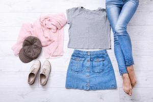 Modern outfit with different accessories and female legs in jeans on white wooden floor. Top view and copy space. photo