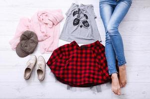 Casual outfit with different accessories and female legs in jeans on white wooden floor. Top view and copy space. photo