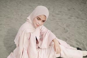 hermosa modelo femenina islámica usando moda hijab, un vestido de novia moderno para mujer musulmana sentada en la arena y la playa. retrata a una modelo asiática usando hiyab divirtiéndose en la playa con árboles foto