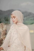 hermosa modelo femenina islámica usando moda hijab, un vestido de novia moderno para mujer musulmana sentada en la arena y la playa. retrata a una modelo asiática usando hiyab divirtiéndose en la playa con árboles foto