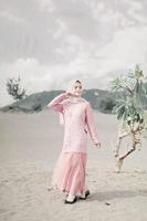 Beautiful islamic female model wearing hijab fashion, a modern wedding dress for muslim woman walks along the sand and the sea. A asian girl model using hijab having fun at the beach. Photo prewedding