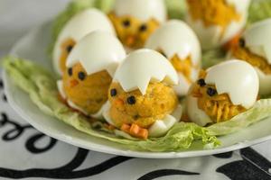 Appetizer of boiled stuffed decorative eggs in the form of small chicks placed on lettuce. Easter decoration. Selective Focus. photo