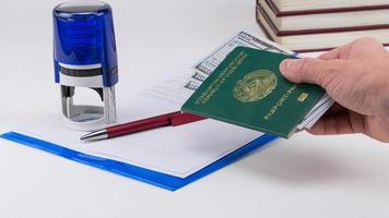 la mano sostiene el pasaporte de uzbekistán con dólares estadounidenses en el fondo de los documentos y el sello de goma. concepto - soborno y corrupción