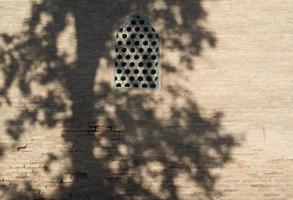 An old brick wall with a window and a shade from a tree. Ancient buildings of medieval Asia. Bukhara, Uzbekistan photo