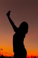 mujer con una actitud positiva frente al fondo del cielo del atardecer. mujer gesticulando éxito - silueta sobre el cielo nocturno foto