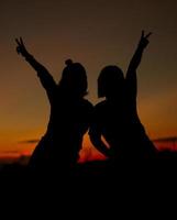 Silhouette of girls make heart with their hand. Happy friendship concept. photo