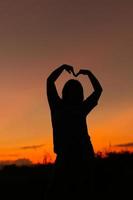 mujer con una actitud positiva frente al fondo del cielo del atardecer. mujer gesticulando éxito - silueta sobre el cielo nocturno foto