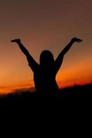 mujer con una actitud positiva frente al fondo del cielo del atardecer. mujer gesticulando éxito - silueta sobre el cielo nocturno foto