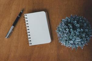 cuaderno en blanco y bolígrafo y flor sobre fondo de mesa de madera vintage.vista superior con espacio de copia. foto