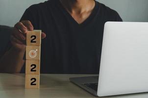 Man holding cube wooden target numeber 2022 Working on a desk with a computer. Business idea. photo