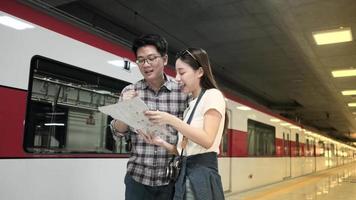 el hombre tailandés ayuda a una hermosa turista asiática a buscar información y encontrar un lugar para viajar en la plataforma de la estación de tren pública, estilo de vida de viaje de pasajeros, transporte informal en vacaciones de viaje. video