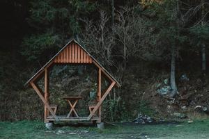 Wooden gazebo on the lawn on a background of forest and mountains. Copy, empty space for text photo