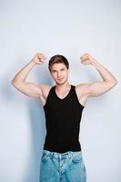 Muscular young man shows biceps in black t-shirt on a white background. Copy, empty space for text photo