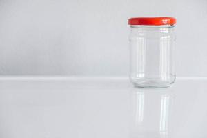 frasco de vidrio vacío con tapa roja sobre fondo blanco de mesa foto