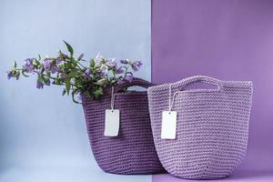 Two purple handmade knitted bag with flowers on a purple and light blue background. Copy, empty space for text photo
