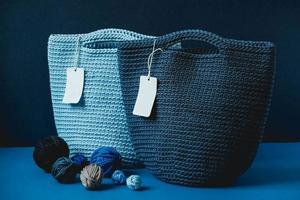 Blue knitted handmade bags with balls of thread on a blue background. Copy, empty space for text photo