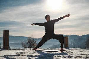 Caucasian senior man doing yoga exercises in front of amazing sunset on the winter mountains. Copy, empty space for text photo