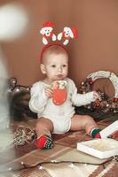 hermoso niñito celebrando la navidad. niño gracioso vestido con un traje de navidad cerca del árbol de navidad en la habitación foto