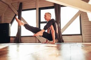 Senior man with a naked torso practicing yoga classic asana training in studio in front of a window. Copy, empty space for text photo