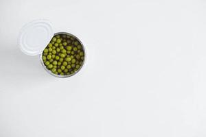 Canned green sweet peas in an open aluminum metal can on a white table. Top view. Copy, empty space for text photo