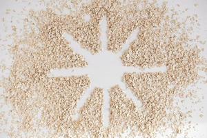 Dry oatmeal scattered in the form of the sun on a white background photo