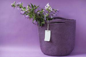 Purple handmade knitted bag with flowers on a purple background. Copy, empty space for text photo