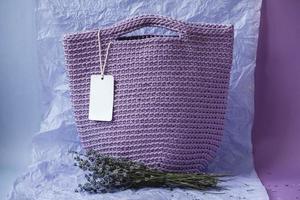Purple handmade knitted bag with flowers on a purple background. Copy, empty space for text photo
