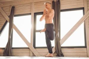 Man with a naked torso practicing yoga training in studio in front of a window. Copy, empty space for text photo