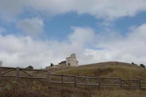 Church of San Pantaleon de la Losa, built on the top of a hill, seen from the pathway that ends there. Wooden fence around the field. Merindades, Burgos, Spain photo