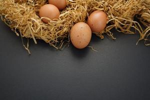 Fresh healthy organic, free-range speckled brown eggs with hay nest flat lay on black background. Negative, copy space for design. photo
