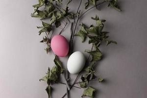 huevos con cáscara de huevo de color rosa y blanco con ramitas de arce secas y hojas planas sobre fondo de color gris crema neutro. foto