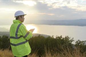 un ingeniero hombre lleva un casco protector en la cabeza, utilizando datos de ingeniería de análisis de tabletas. foto