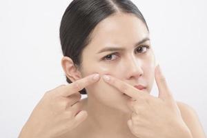 portrait of young beautiful woman is checking her skin and popping pimple over white background studio photo