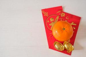 Chinese New Year festival concept.  Mandarin oranges and gold ingots on red envelopes with white wooden background. photo