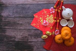 Chinese New Year festival concept. Mandarin oranges, red envelopes, gold ingots and tea pot on red cloth with old wooden background. Chinese character fu which stands for luck