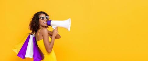 mujer feliz y hermosa con bolsas de compras y megáfono en un fondo de banner amarillo colorido aislado para conceptos de venta y descuento foto