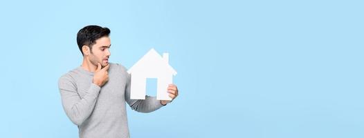 Young man looking at house model and thinking isolated on light blue banner background with copy space photo